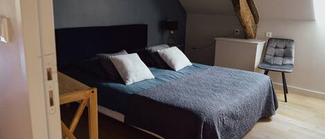 Une chambre à coucher avec un lit, une table de chevet en bois, une chaise et un grand tronc d’arbre adossé au mur.