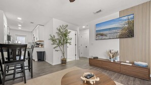 A modern living room with a dining area, a large painting, and a wooden sideboard.