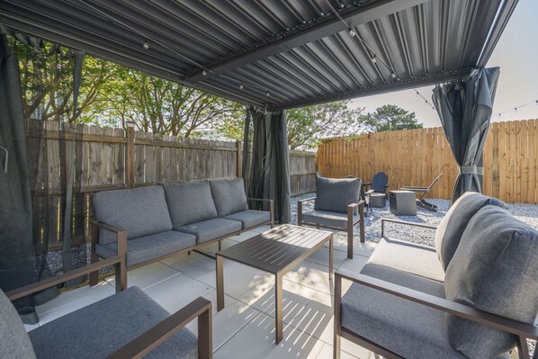 Un patio exterior con zona de estar cubierta, una mesa y una parrilla.