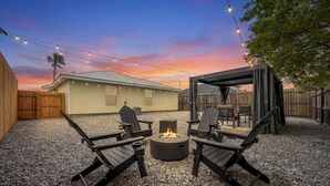 A backyard with a fire pit, two Adirondack chairs, and a covered patio area.