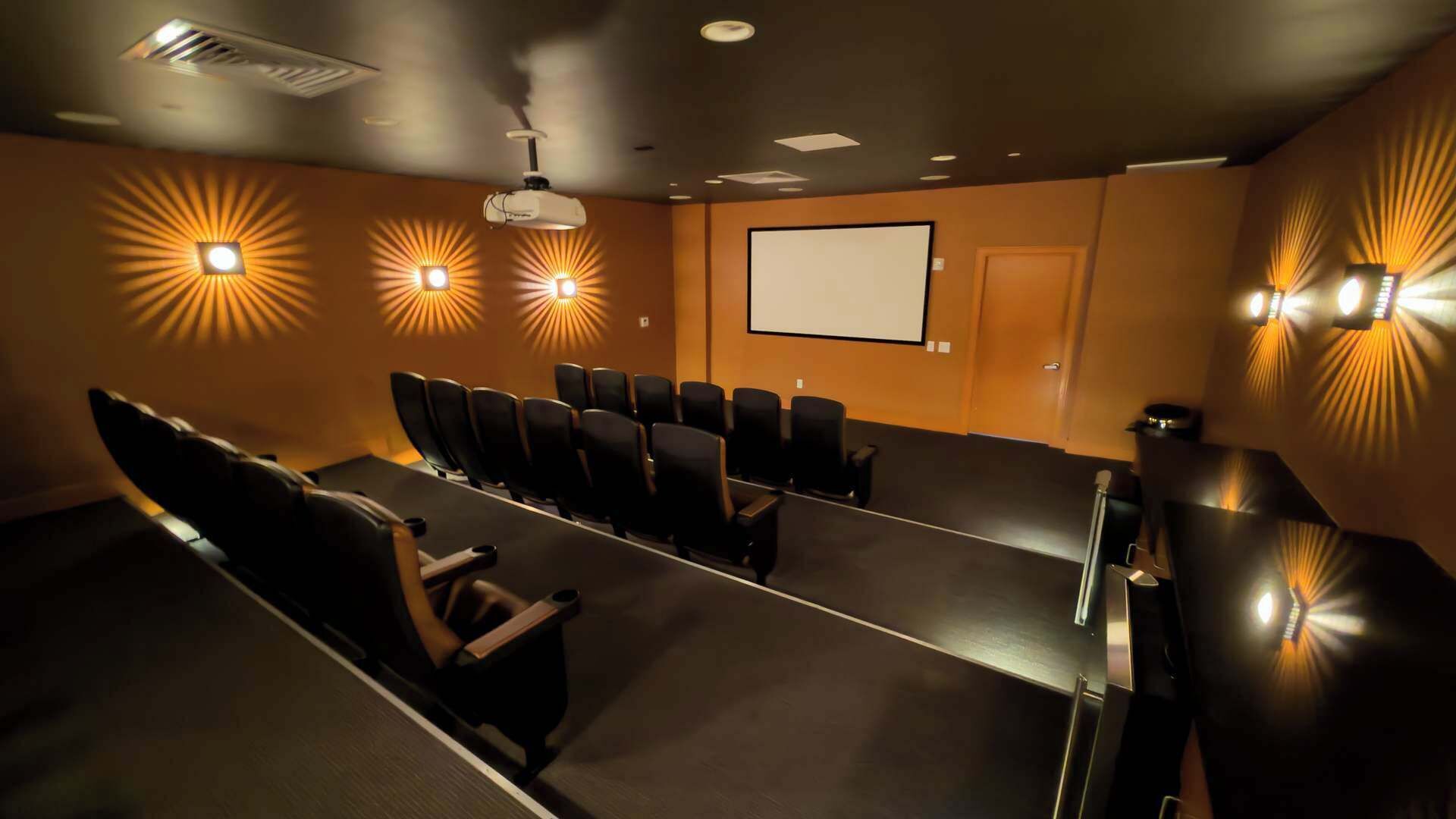Ett konferensrum med rader av stolar, en projektorduk och väggmonterade lampor.