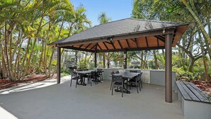 Eine einladende Terrassengaststätte mit Tischen und Stühlen, umgeben von üppigem Grün und einem überdachten Bereich mit Ziegeldach.