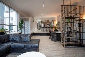 A modern living room with a leather sofa, a dining area with chairs, and a decorative metal shelf. - Loft w/ Glass Ceiling, Pool & Tennis, Surfers (Surfers Paradise)