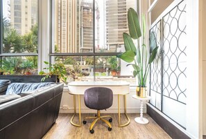A modern room with a leather sofa, a desk with a chair, large windows, and a view of tall buildings. - Loft w/ Glass Ceiling, Pool & Tennis, Surfers (Surfers Paradise)