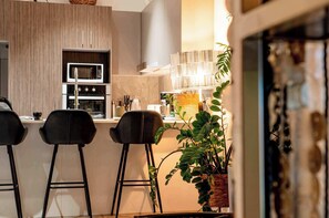 A modern kitchen with bar stools, a microwave, oven, and a potted plant. - Loft w/ Glass Ceiling, Pool & Tennis, Surfers (Surfers Paradise)