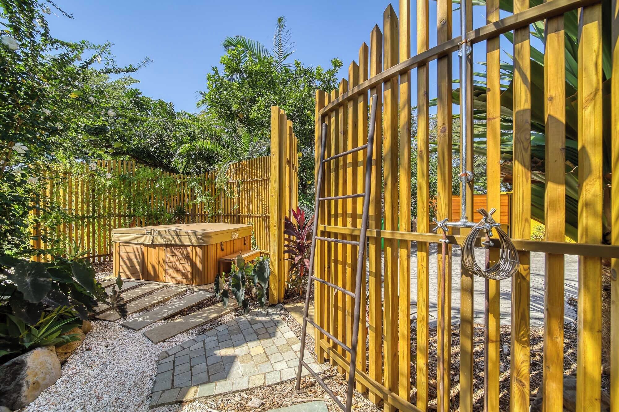 A wooden fence with a gate, a hot tub, and a stone pathway.