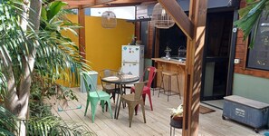 A patio area with a wooden table and chairs, a refrigerator, and potted plants. - L'Oasis des Colibris – Tiny House & Spa in L'Étang-Salé (L'Étang-Salé)