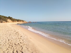 A sandy beach with footprints, a clear sky, and distant rocky formations.