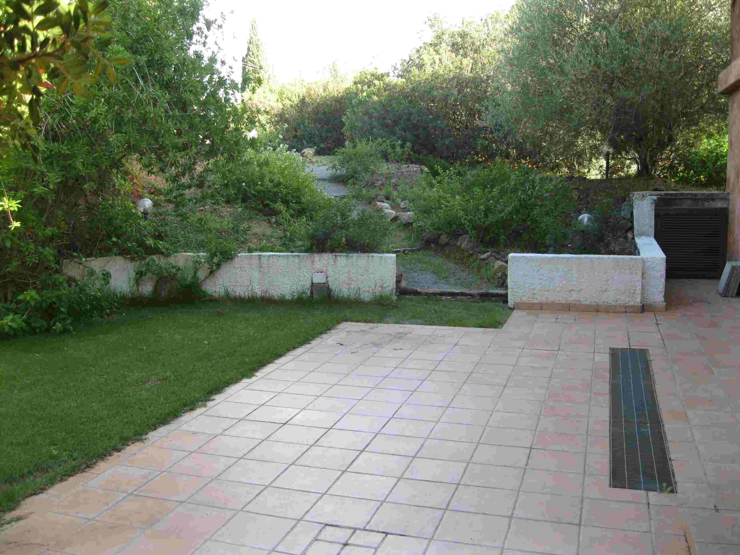 A paved patio area with a grassy lawn and a stone wall.