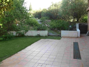 Une terrasse dallée, avec une pelouse et un mur en pierre.