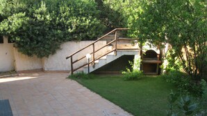 Un patio con piso de baldosas, una escalera de madera y un muro de piedra.