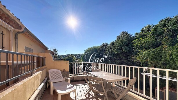 Ein Balkon mit Tisch und Stühlen, einem Geländer und Blick auf Bäume sowie ein Gebäude im Hintergrund.