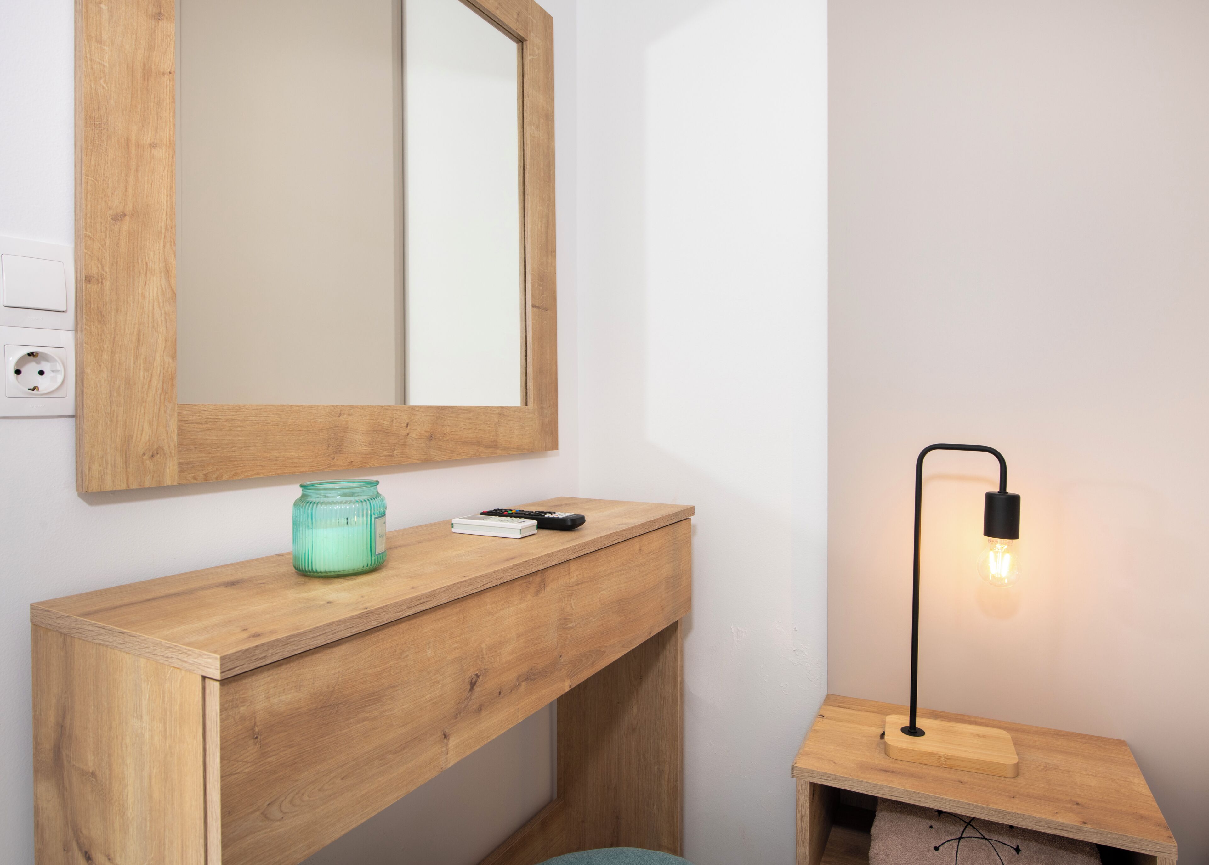 A wooden vanity with a mirror, a candle, and a remote control.