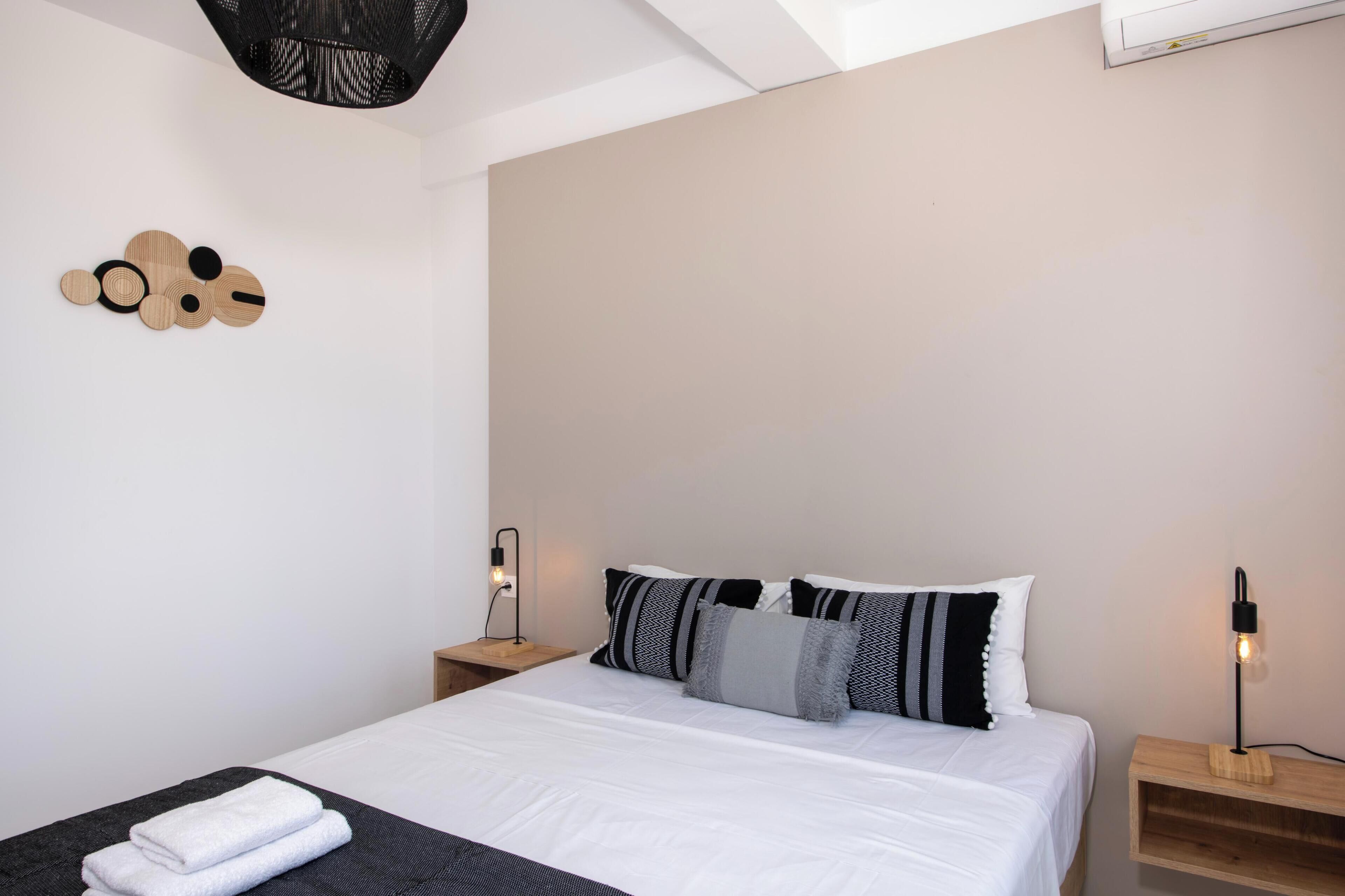 A neatly made bed with white linens, a bedside table with a lamp, and a wall-mounted light fixture.