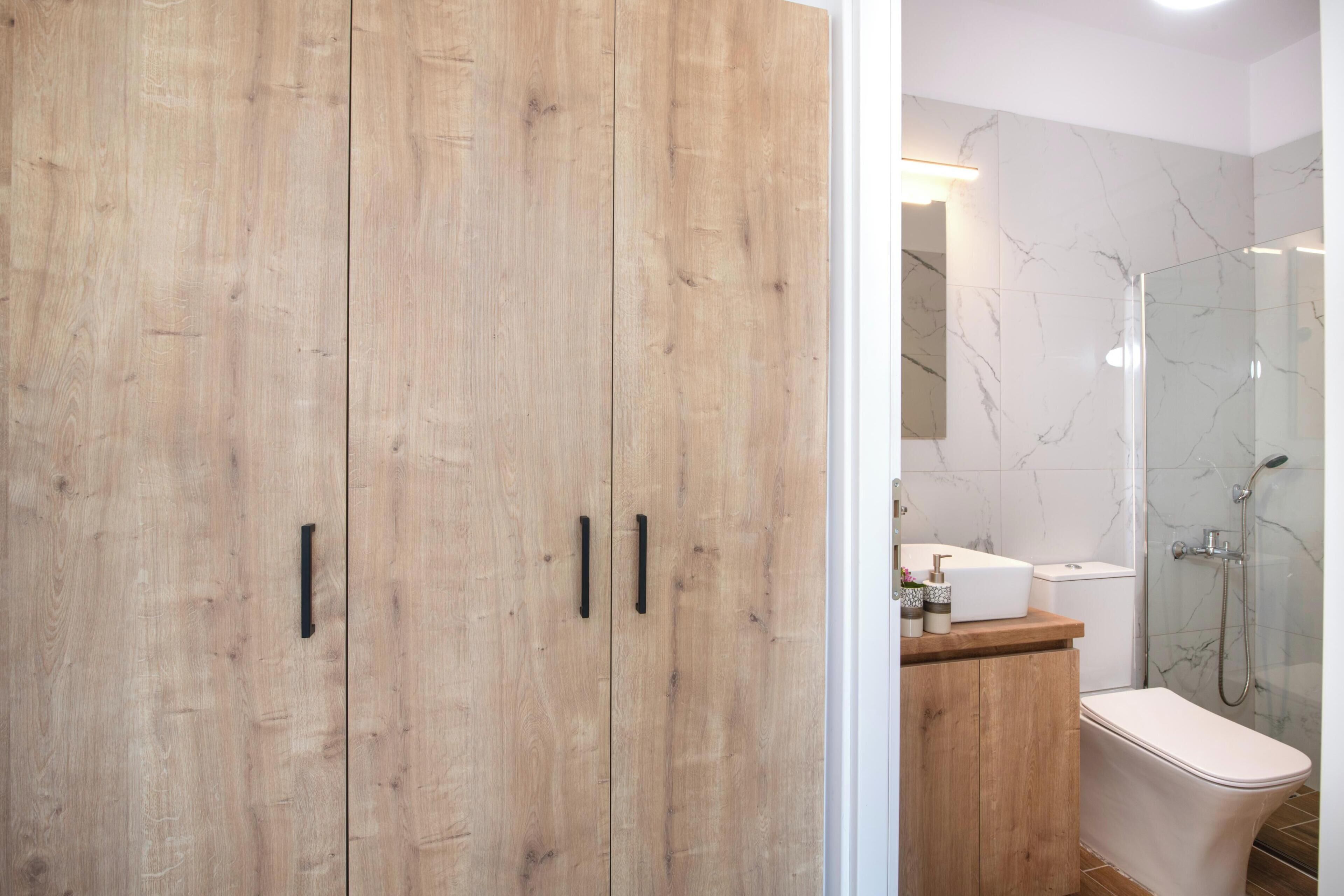 Une salle de bain moderne avec des meubles en bois, un mur de douche en marbre et des toilettes blanches.