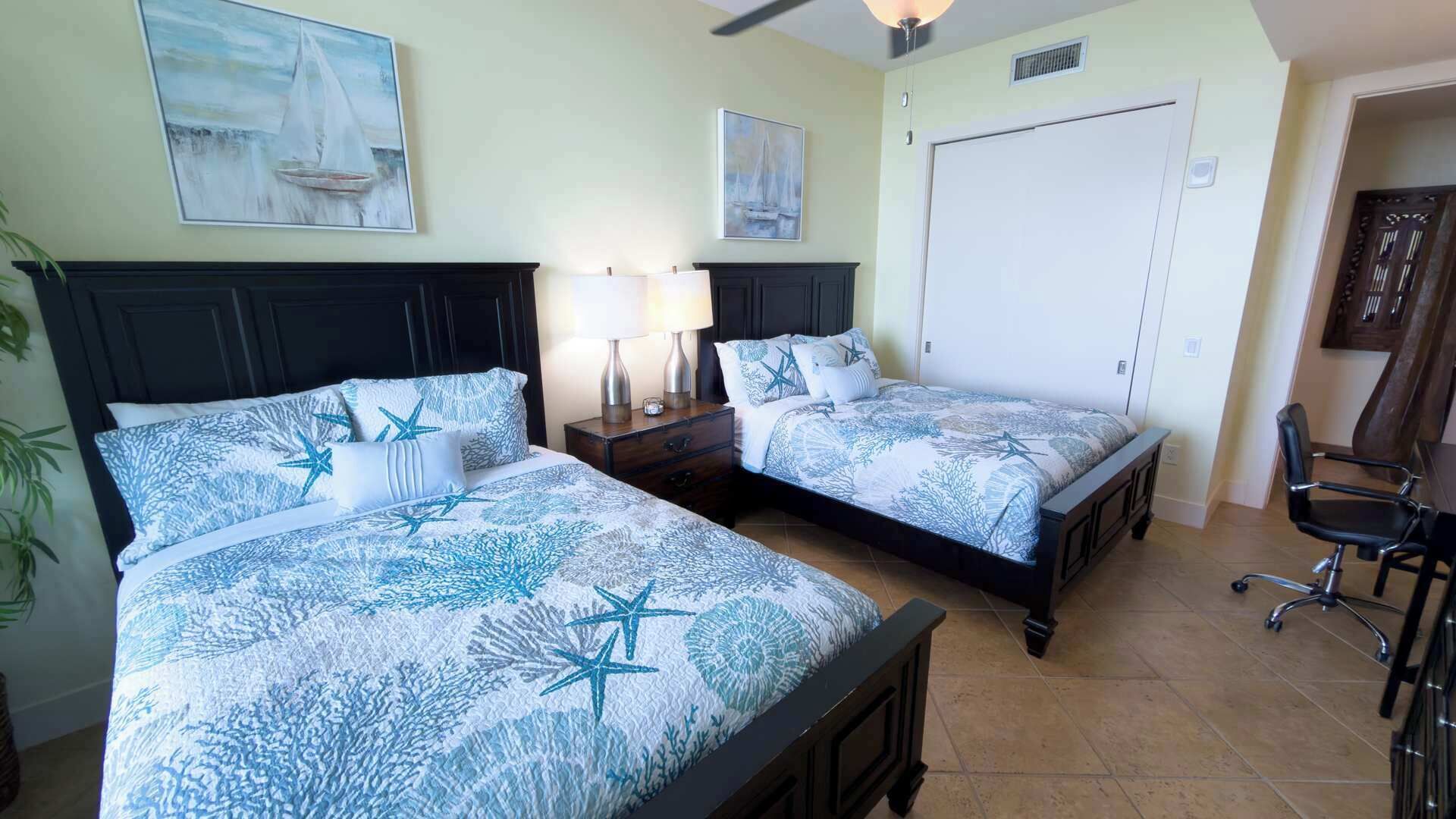 A bedroom with two beds, a desk, a chair, and artwork on the walls.