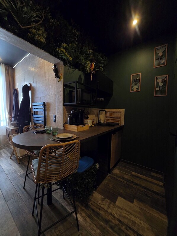 Un comedor acogedor con una mesa redonda y sillas de mimbre, un microondas, y una pequeña zona de cocina con mostrador y armarios.