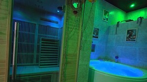 Una stanza spa con una vasca da bagno ampia, un box doccia in vetro e una parete illuminata di verde.