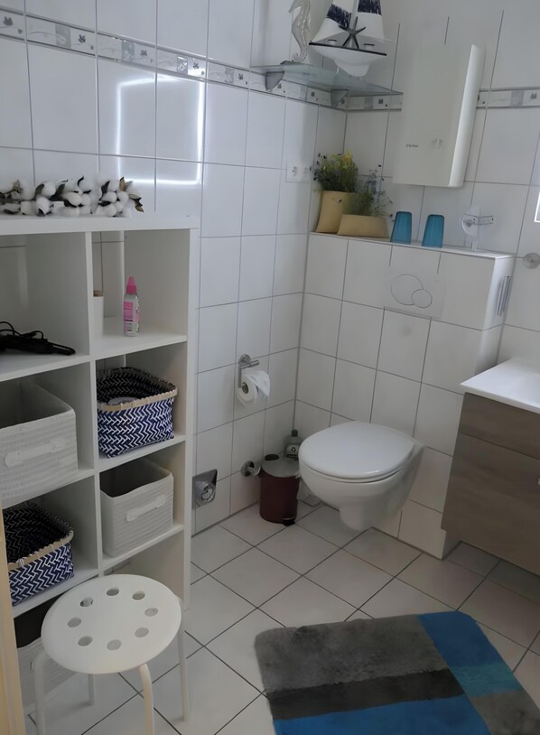 Un baño con inodoro, estantes con cestas, un cubo de basura y un taburete pequeño.
