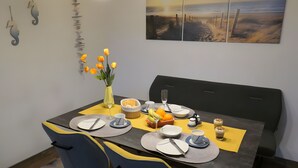 Una mesa de comedor dispuesta con platos, cubiertos, un florero con flores y un frutero.