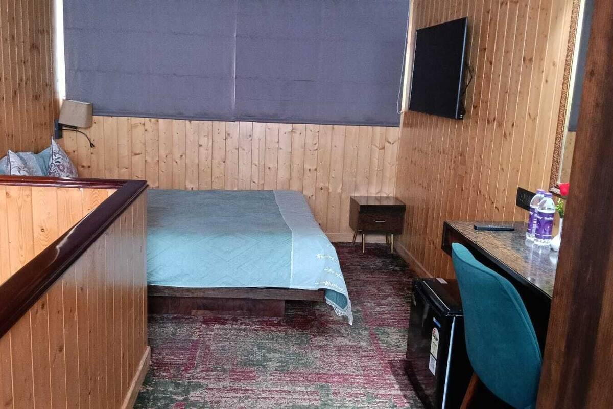 Ein kleines Hotelzimmer mit Bett, Schreibtisch, Stuhl, Fernseher und Fenster.