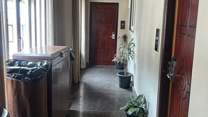 Un couloir avec un plafond en bois, une poubelle, des plantes en pot et une porte avec une plaque numérotée.