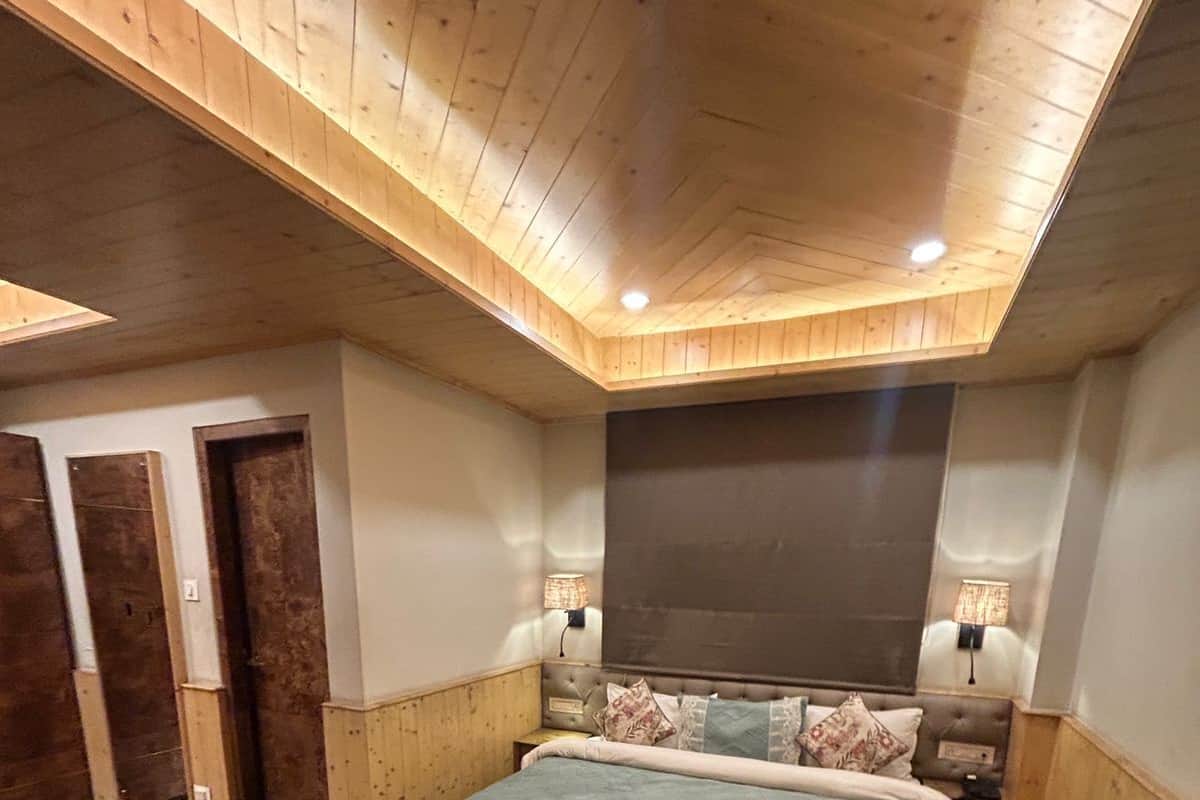 Ein Schlafzimmer mit Holzbalkendecke, einem Bett mit gemustertem Überwurf, zwei Nachttischlampen und einem großen Fenster.