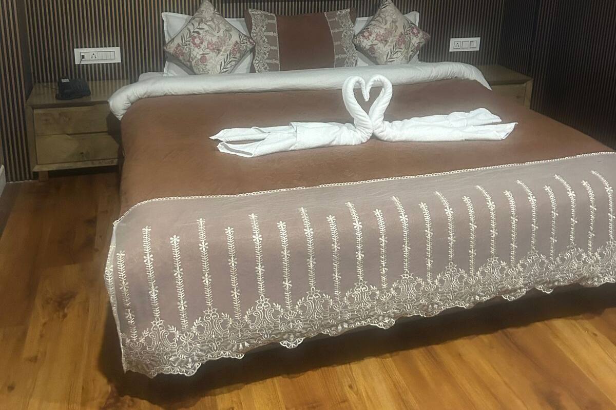 Ein Hotelzimmer mit einem großen Bett, Holzboden, einem Nachttisch mit Lampe und einer Wandleuchte.
