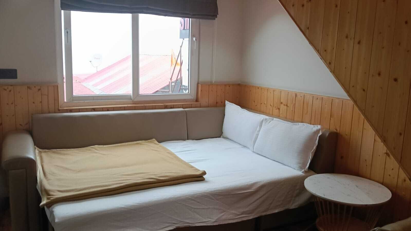Ein Zimmer mit einem Bett, einem runden Tisch und einem Fenster mit Blick auf ein Gebäude.