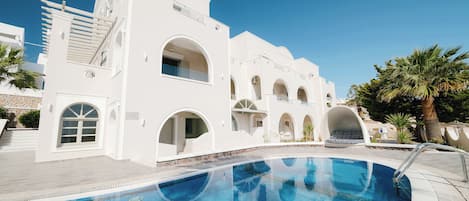 A white building with a pool, arched windows, and a clear blue sky.