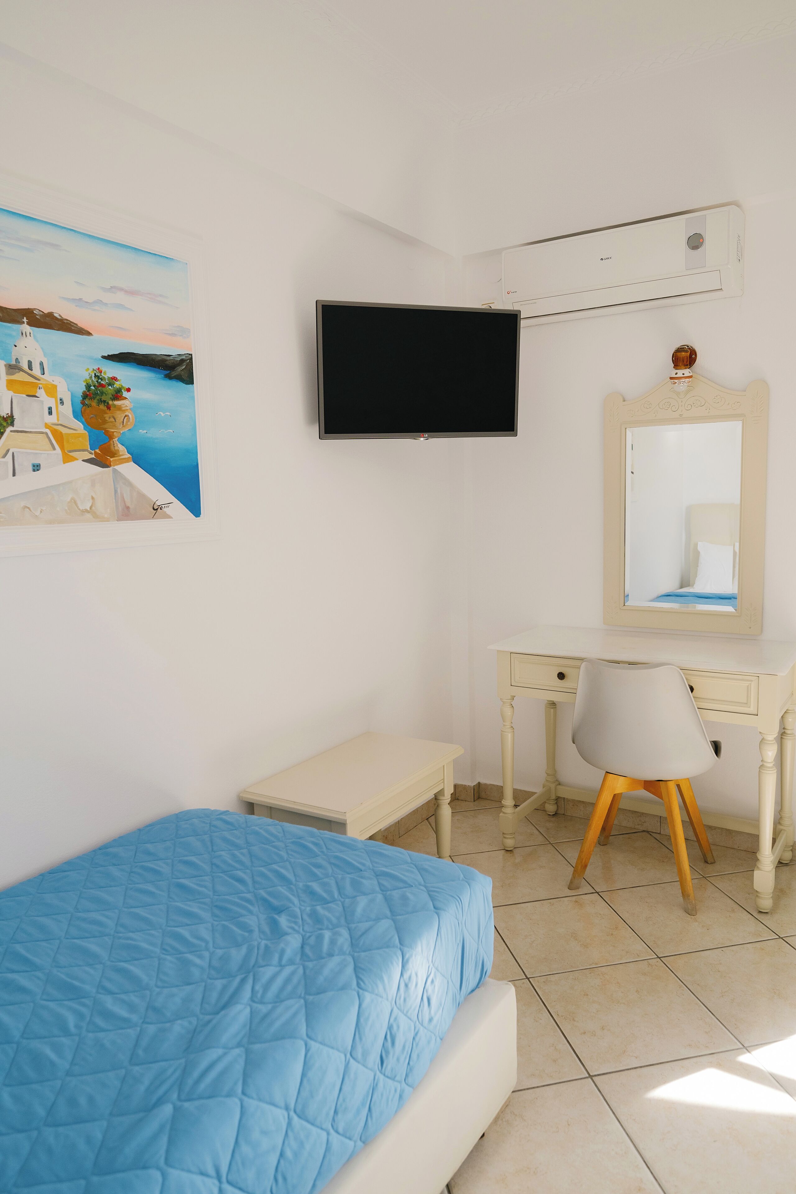 Un dormitorio con una cama, un escritorio, una silla, un televisor, un espejo y un cuadro en la pared.