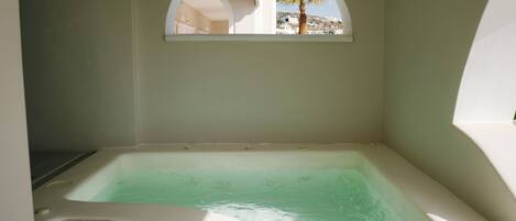 Una bañera con vistas a una palmera y edificios a través de una ventana en arco.