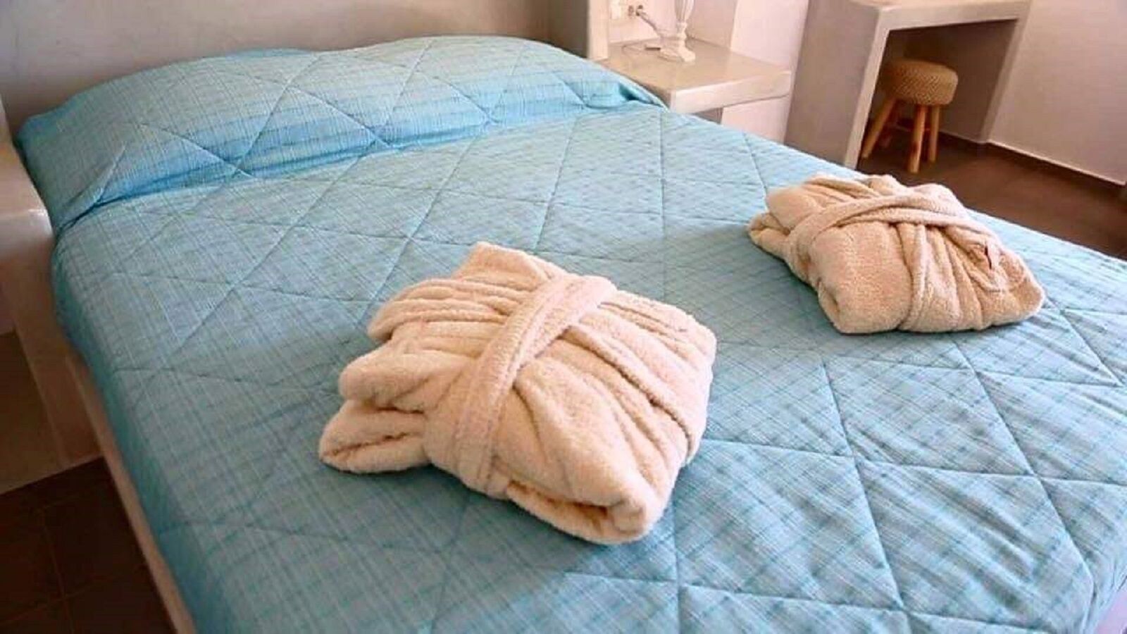 A bed with a blue quilt and two towels.
