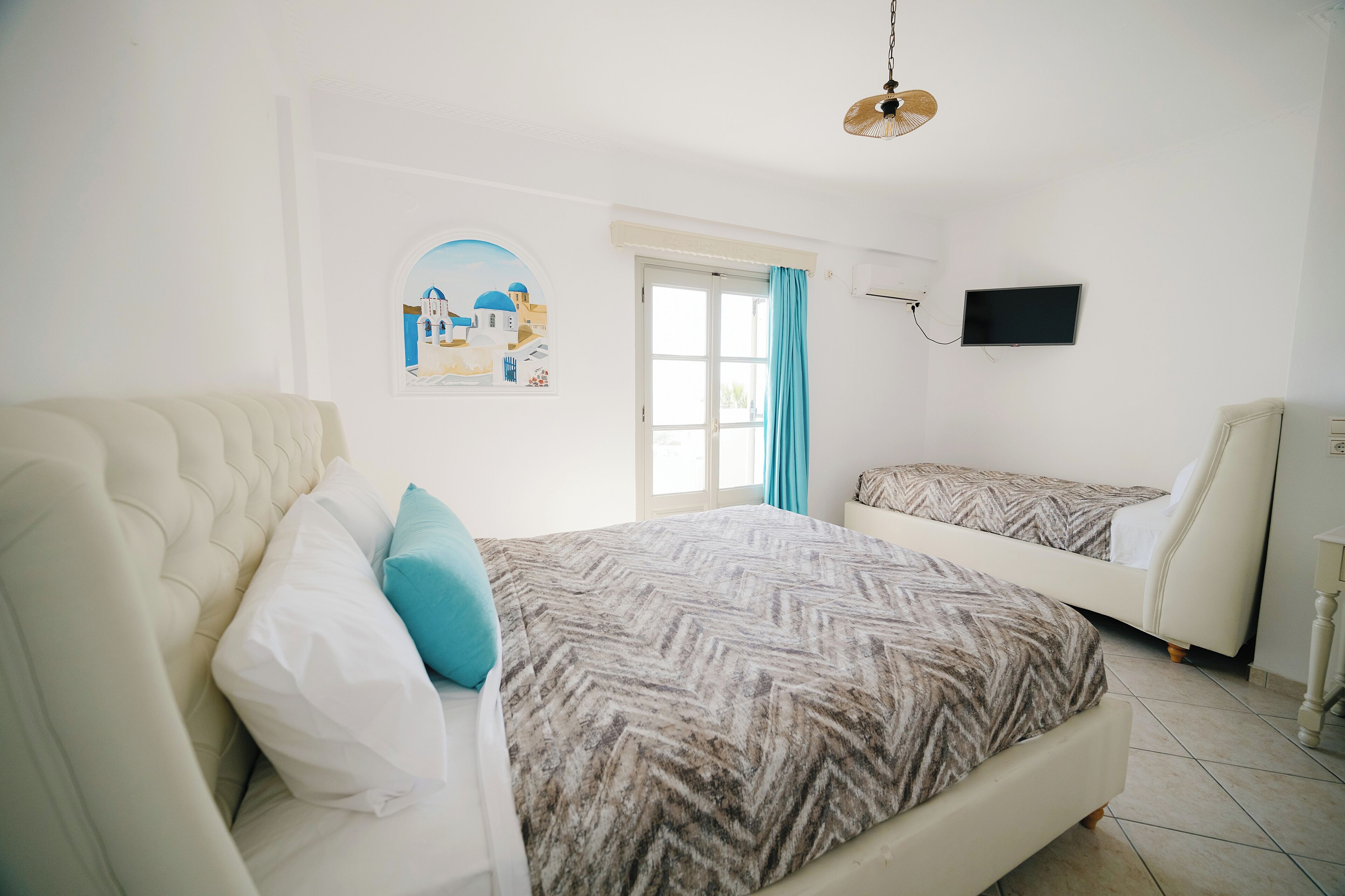 Een slaapkamer met een groot bed, een kleiner bed, een televisie en een raam met gordijnen.
