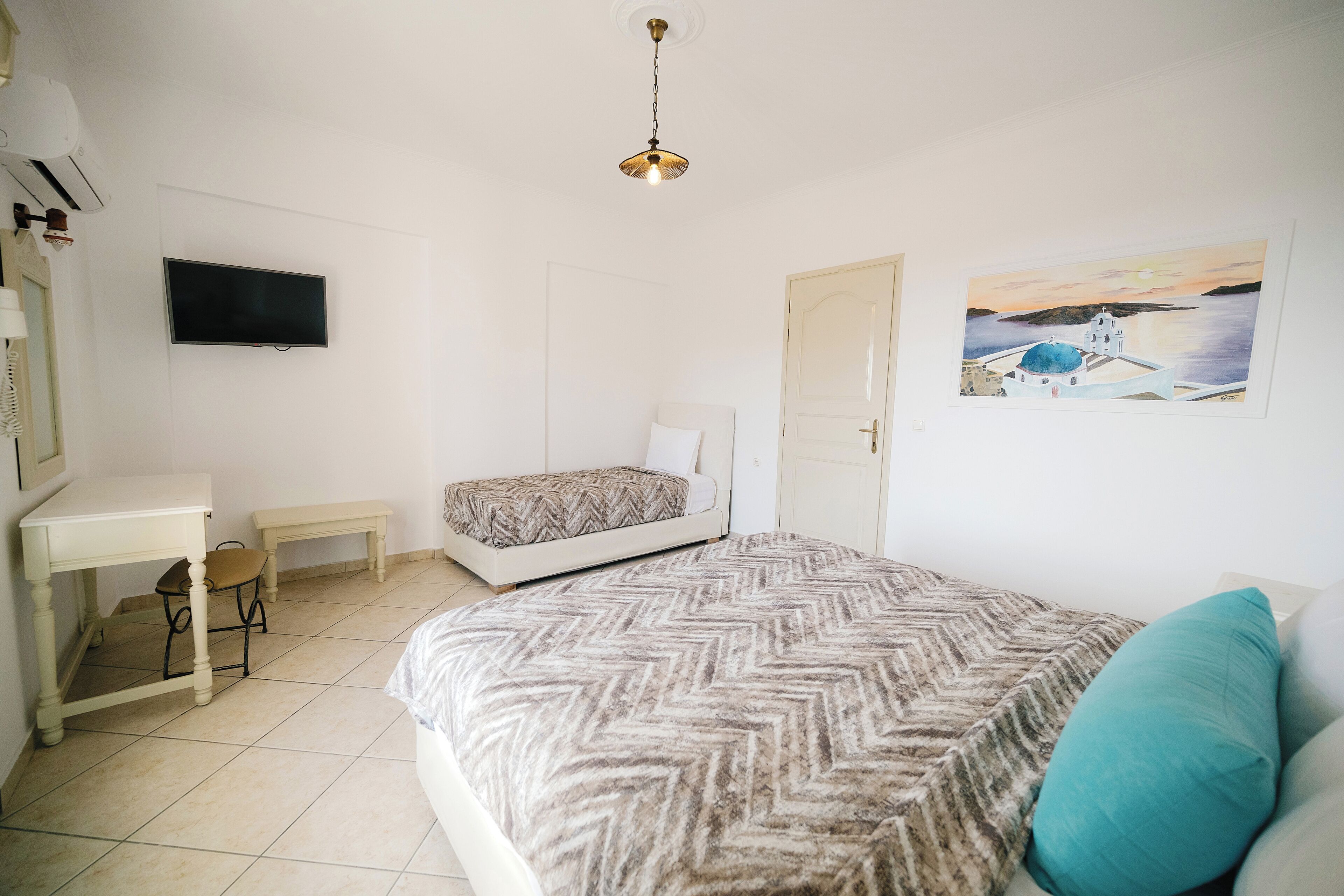 A bedroom with a bed, a desk, a chair, a television, and a door.