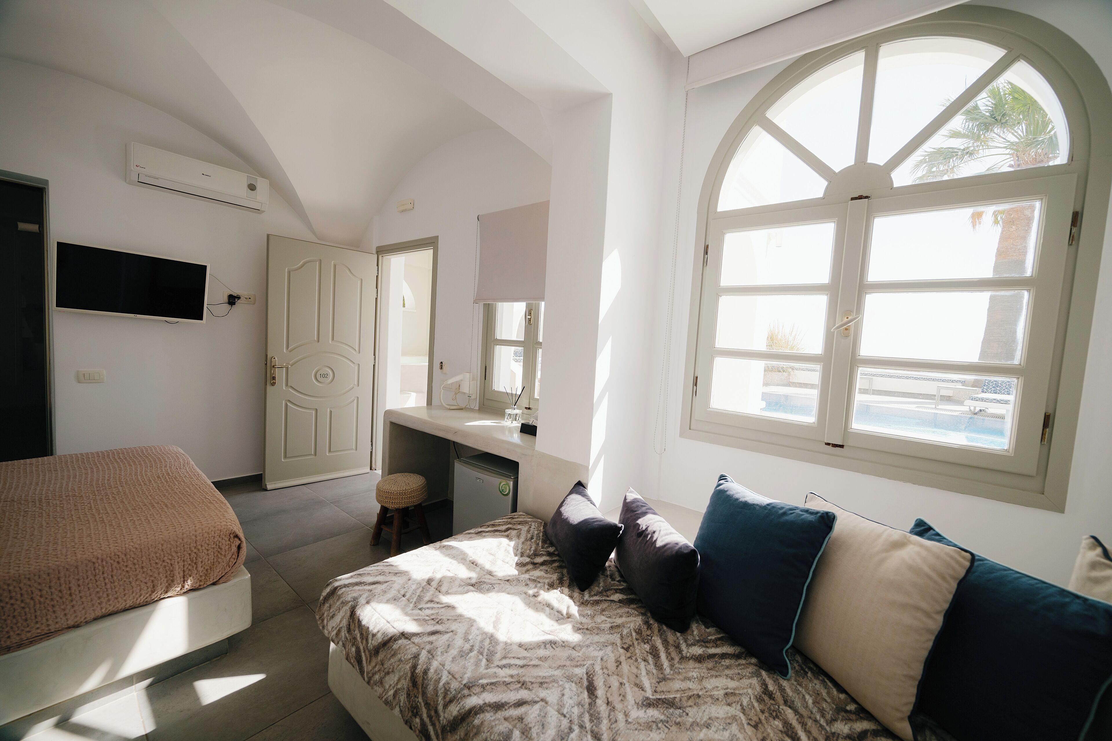 Un dormitorio con cama, escritorio y un amplio ventanal de arco.