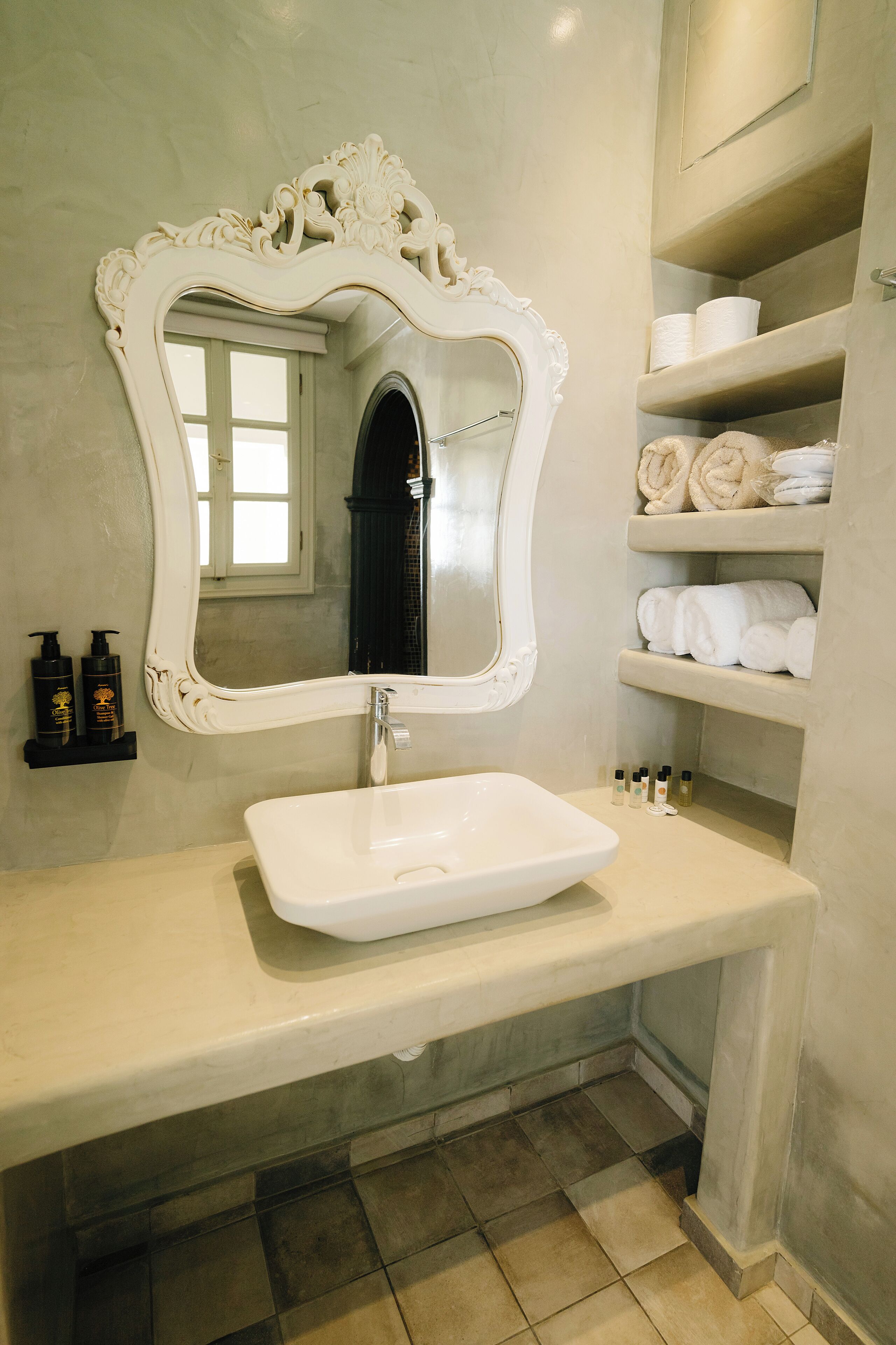 A bathroom with a white vanity, a large ornate mirror, and shelves with towels and toiletries.