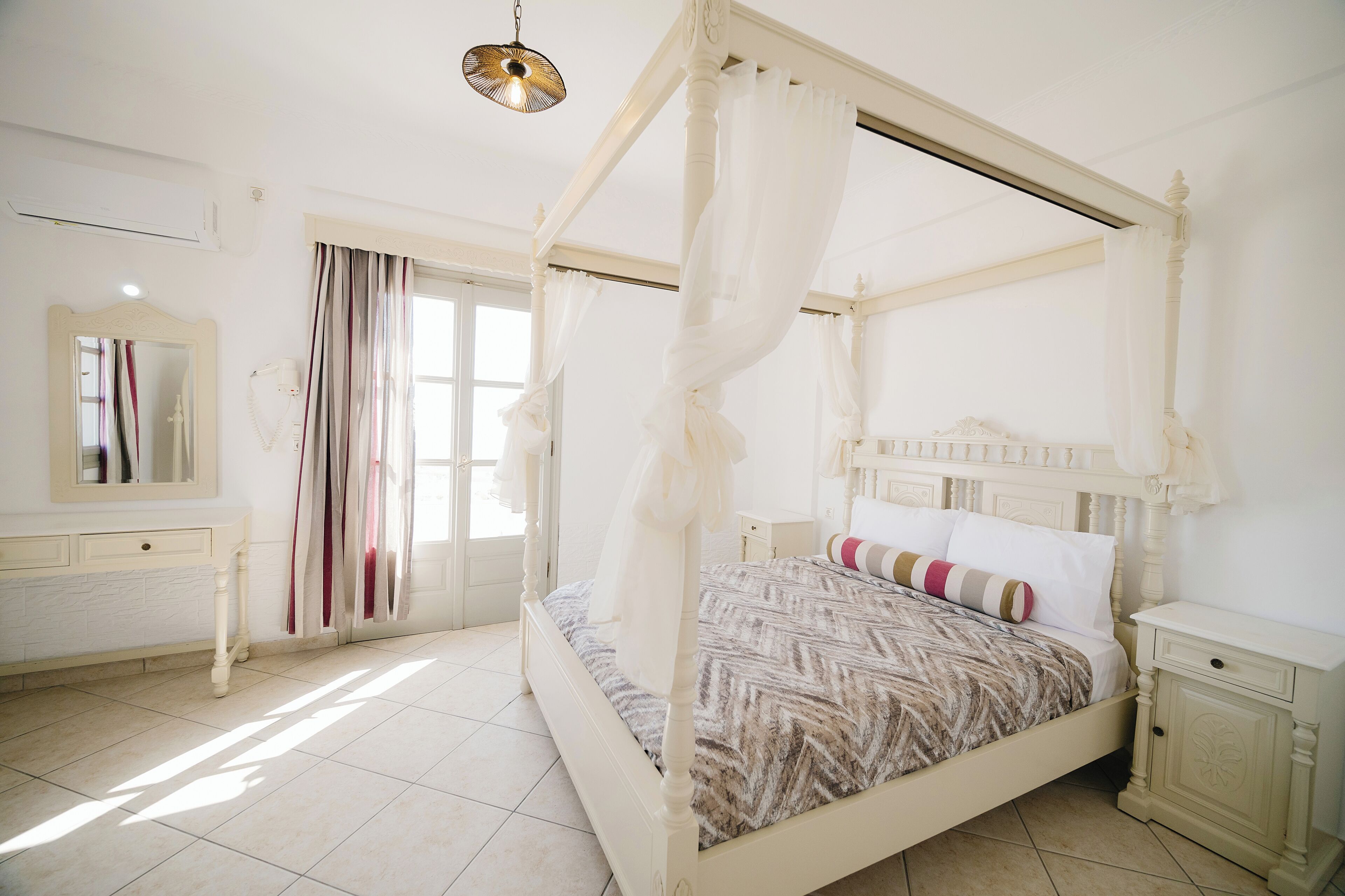 Una cama con dosel, una mesita de noche, un espejo y una ventana con cortinas.