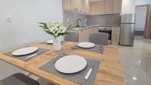 A modern kitchen with wooden cabinets, a stainless steel refrigerator, and a dining area with a wooden table set for four. - Mpia House by RentalsPro (Nea Moudania)