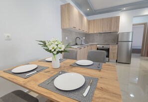 A modern kitchen with wooden cabinets, a stainless steel refrigerator, and a dining area with a wooden table set for four. - Mpia House by RentalsPro (Nea Moudania)