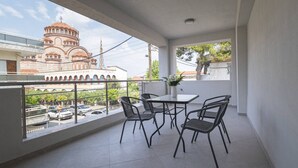 A balcony with a table and chairs, a vase with flowers, and a view of a historic building. - Mpia House by RentalsPro (Nea Moudania)