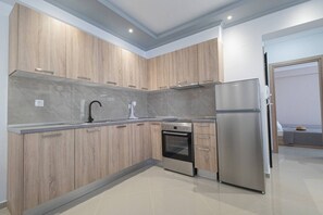 A modern kitchen with wooden cabinets, a stainless steel refrigerator, a built-in oven, and a sink with a faucet. - Mpia House by RentalsPro (Nea Moudania)