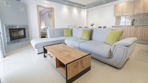 A modern living room with a sectional sofa, a wooden coffee table, and a fireplace. - Mpia House by RentalsPro (Nea Moudania)
