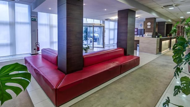 A modern lobby with a red seating area, large pillars, and a reception desk. - HOTEL CAPITAL (Rovigo)