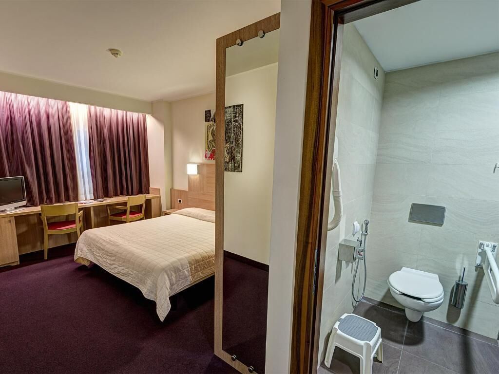A hotel room with a bed, desk, chair, and a bathroom with a toilet and shower.