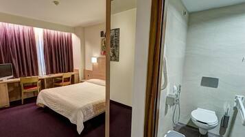 Habitación de hotel con cama, escritorio, silla y baño privado con inodoro y ducha.