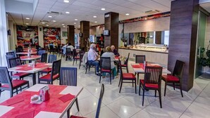 A spacious indoor dining area with multiple tables and chairs, a counter with a display case, and a tiled floor. - HOTEL CAPITAL (Rovigo)