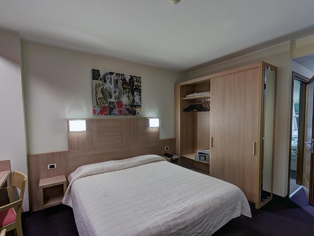 Ett hotellrum med en säng, ett skrivbord, en garderob och en affisch på väggen.