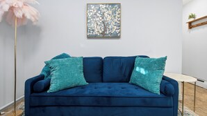 Una sala de estar moderna con un sofá azul oscuro, cojines color turquesa y una obra de arte enmarcada de un árbol en la pared.