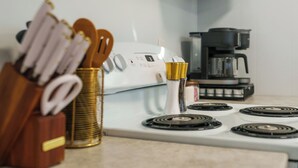 Una cocina con estufa, cafetera y utensilios.